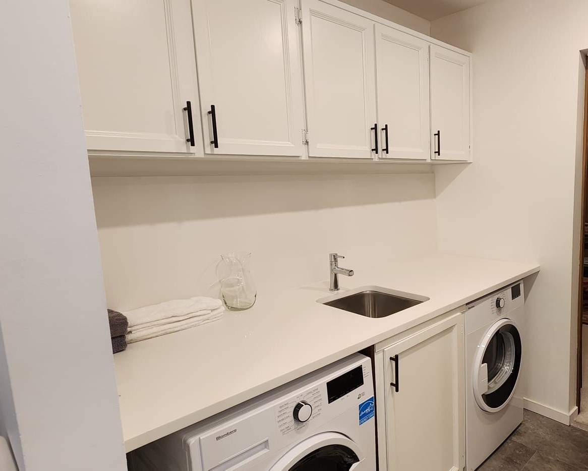 Laundry room after renovation — white cabinetry and quartz counter